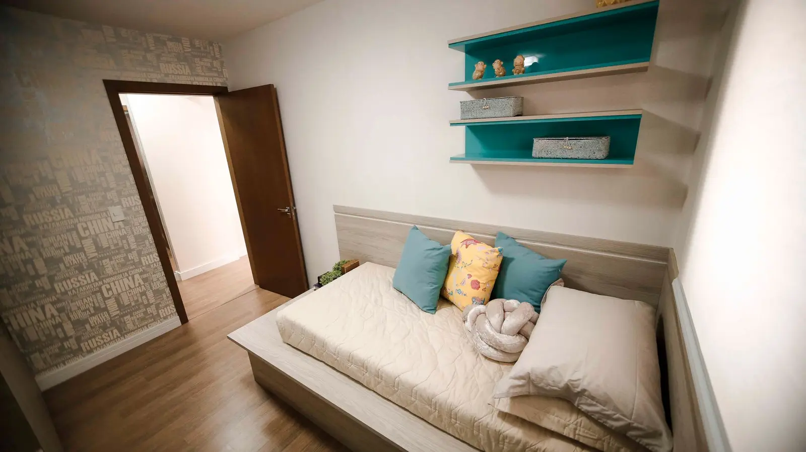 Quarto com cama baixa, almofadas coloridas e prateleiras azuis