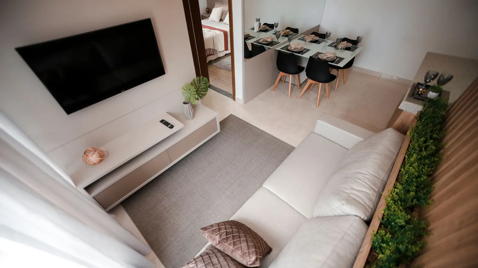 Sala com sofá claro, TV e mesa de jantar ao fundo