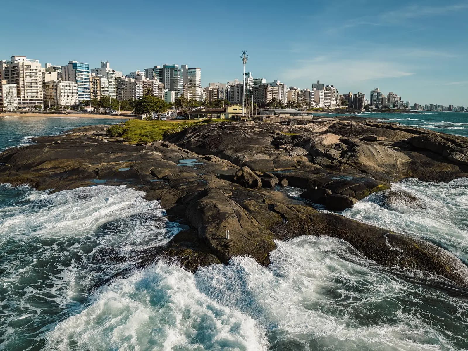 Praia de Guarapari com ondas nas pedras e a cidade ao fundo