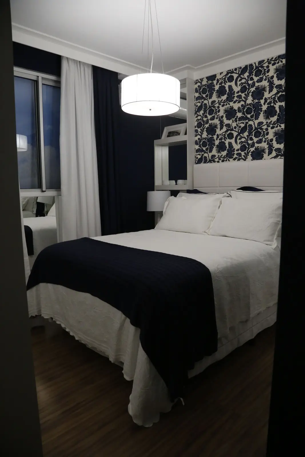 Quarto de casal com roupa de cama clara e cabeceira estampada