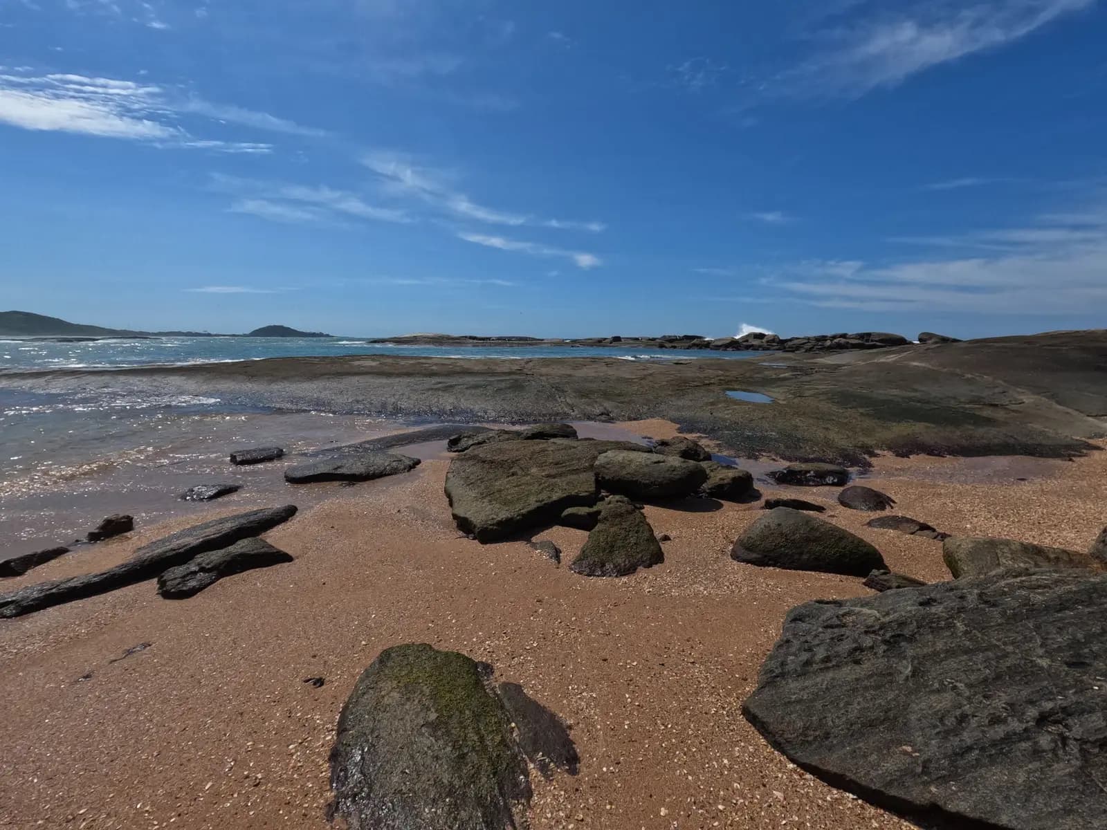 Praia de pedras em Guarapari, com o mar calmo e céu azul