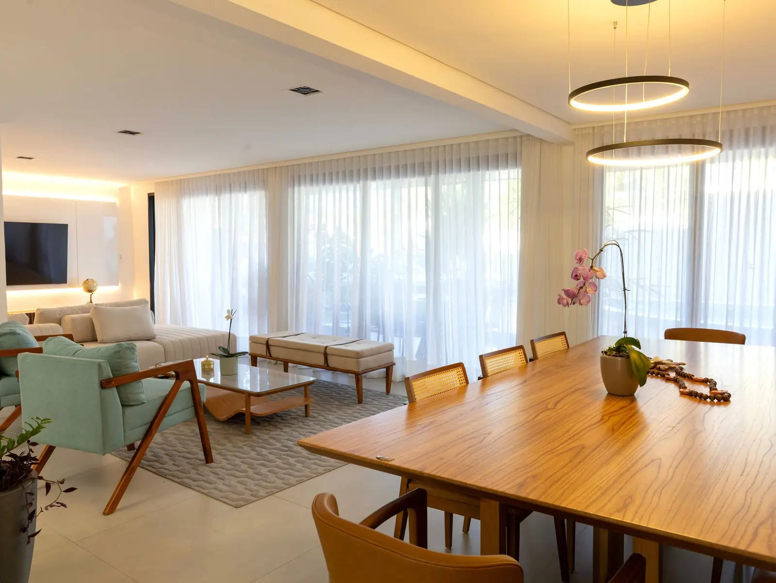 Estar e jantar integrados, com cortinas claras e mesa de madeira