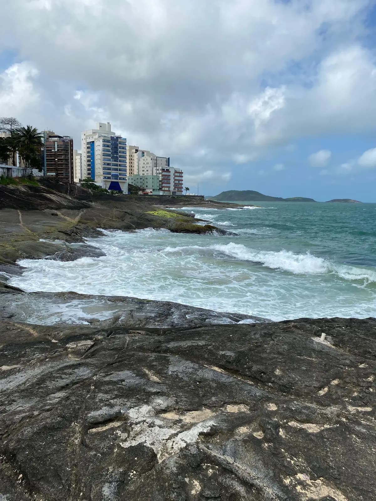 Costão de pedras na Praia das Virtudes, em Guarapari, com os prédios ao fundo