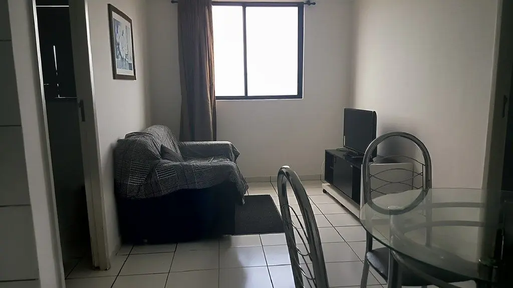 Sala com sofá, TV, mesa de vidro e piso frio
